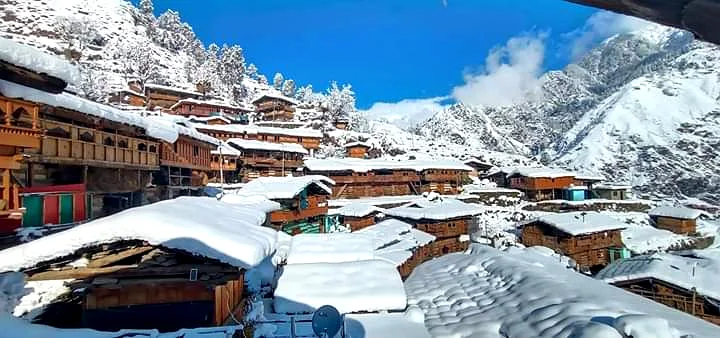 Traditional wood-and-stone Himalayan village rooftops blanketed in fresh snow with mountains behind