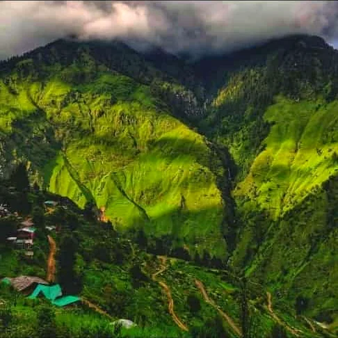 Vivid green Himalayan valley with a winding road, cloud-draped peaks and a small hillside village
